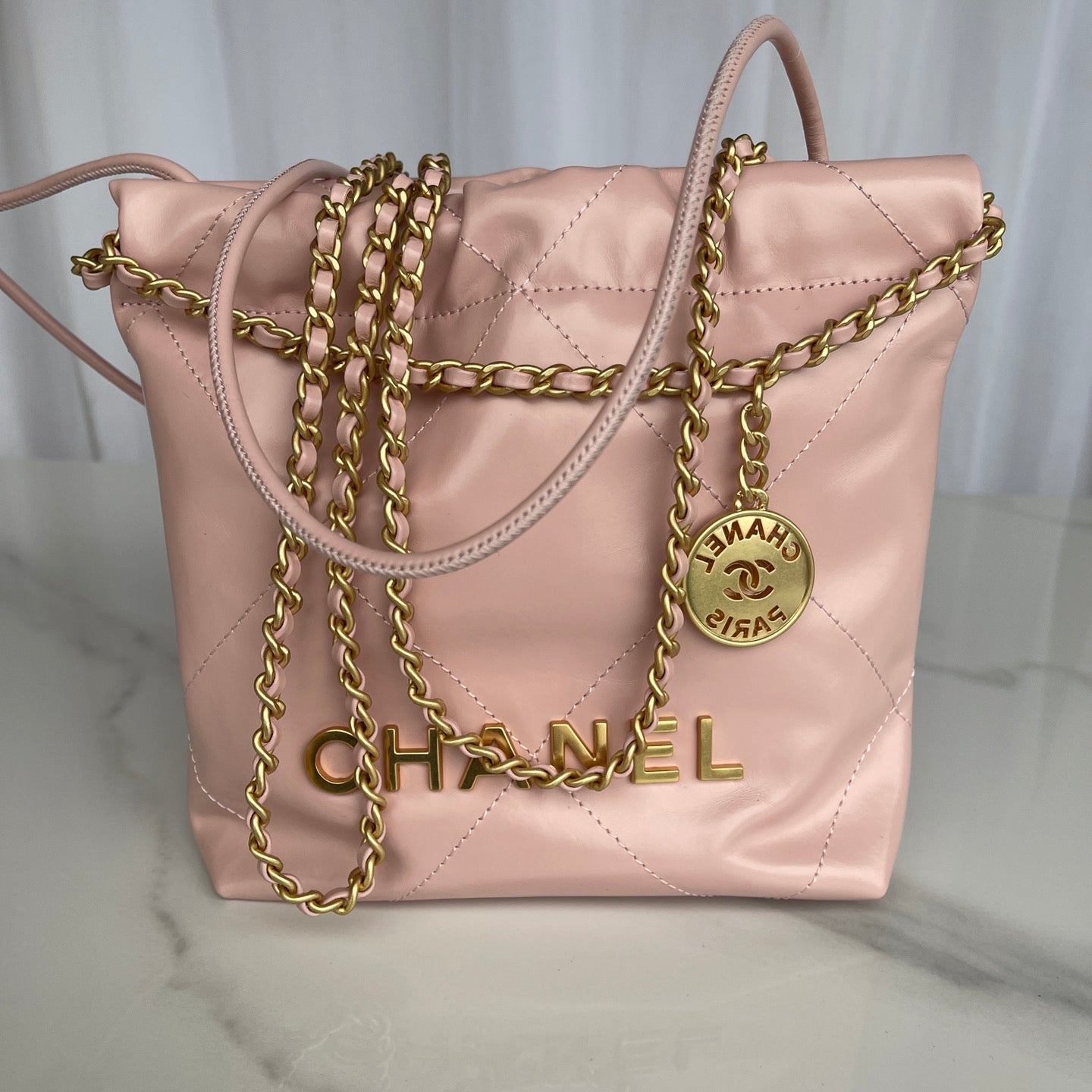 Pink Chanel handbag with gold chain and logo on a light background