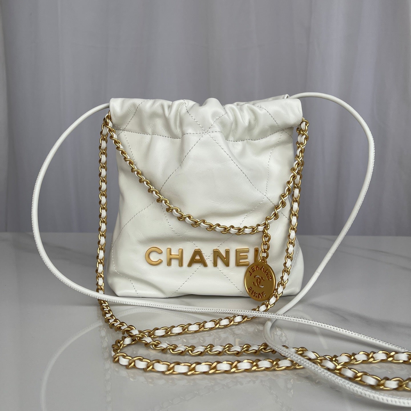 White Chanel handbag with gold chain on a gray background