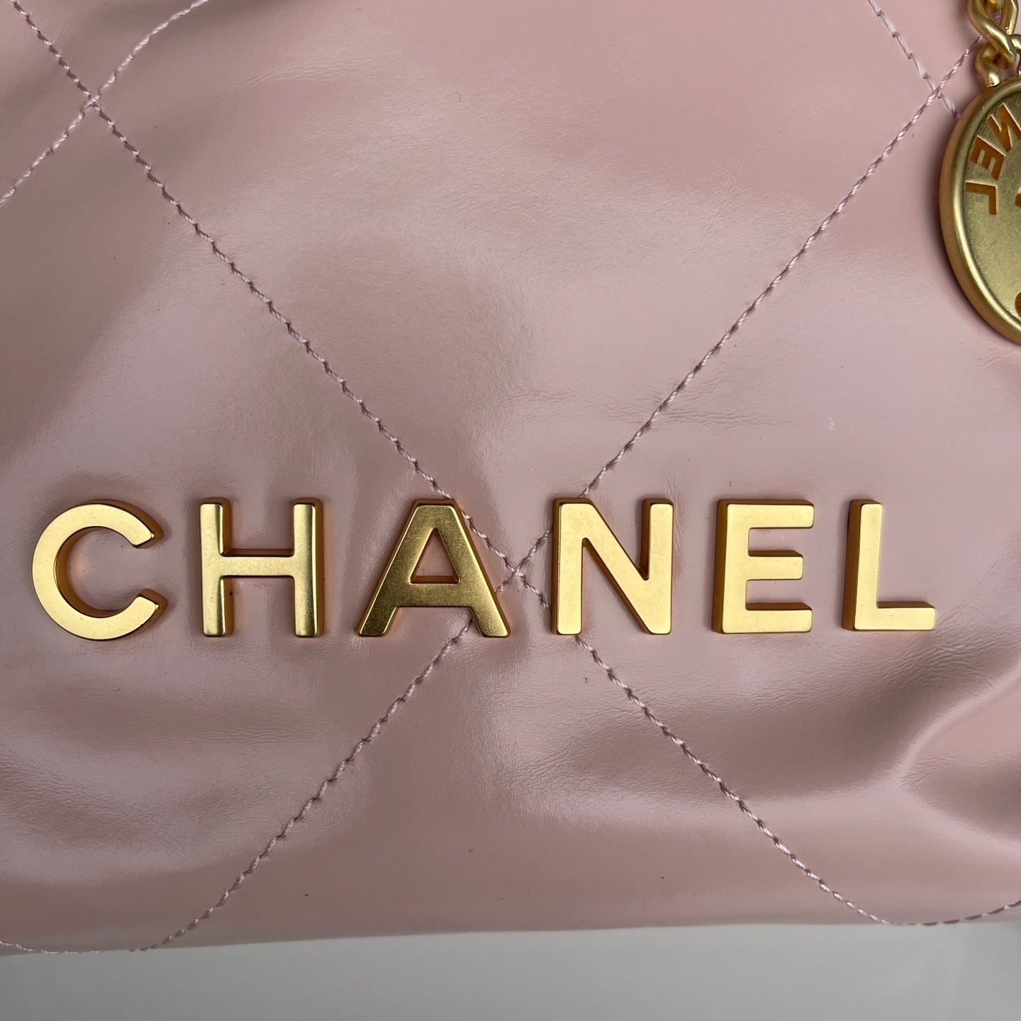 Close-up of a Chanel handbag with gold lettering on a pink quilted leather surface.