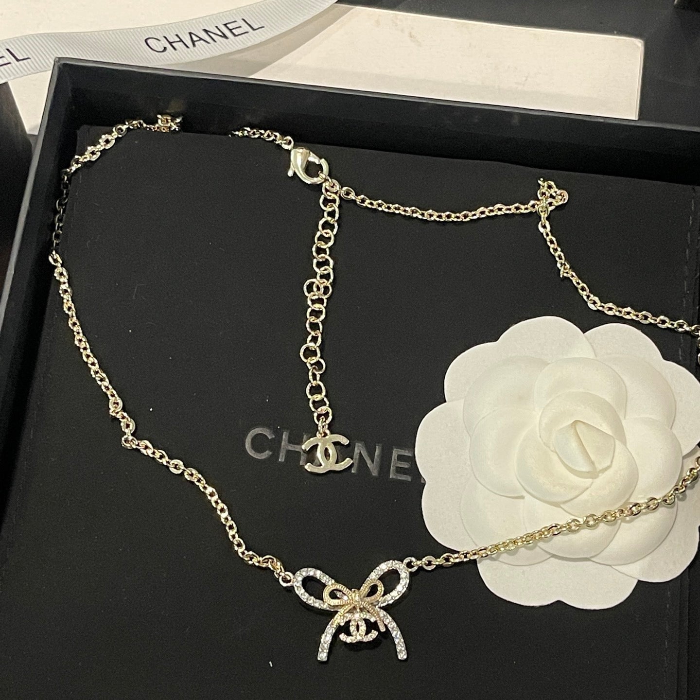 Chanel necklace with bow charm on a black Chanel box with white rose