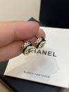 Gold Chanel earrings held by a hand on a Chanel jewelry box.