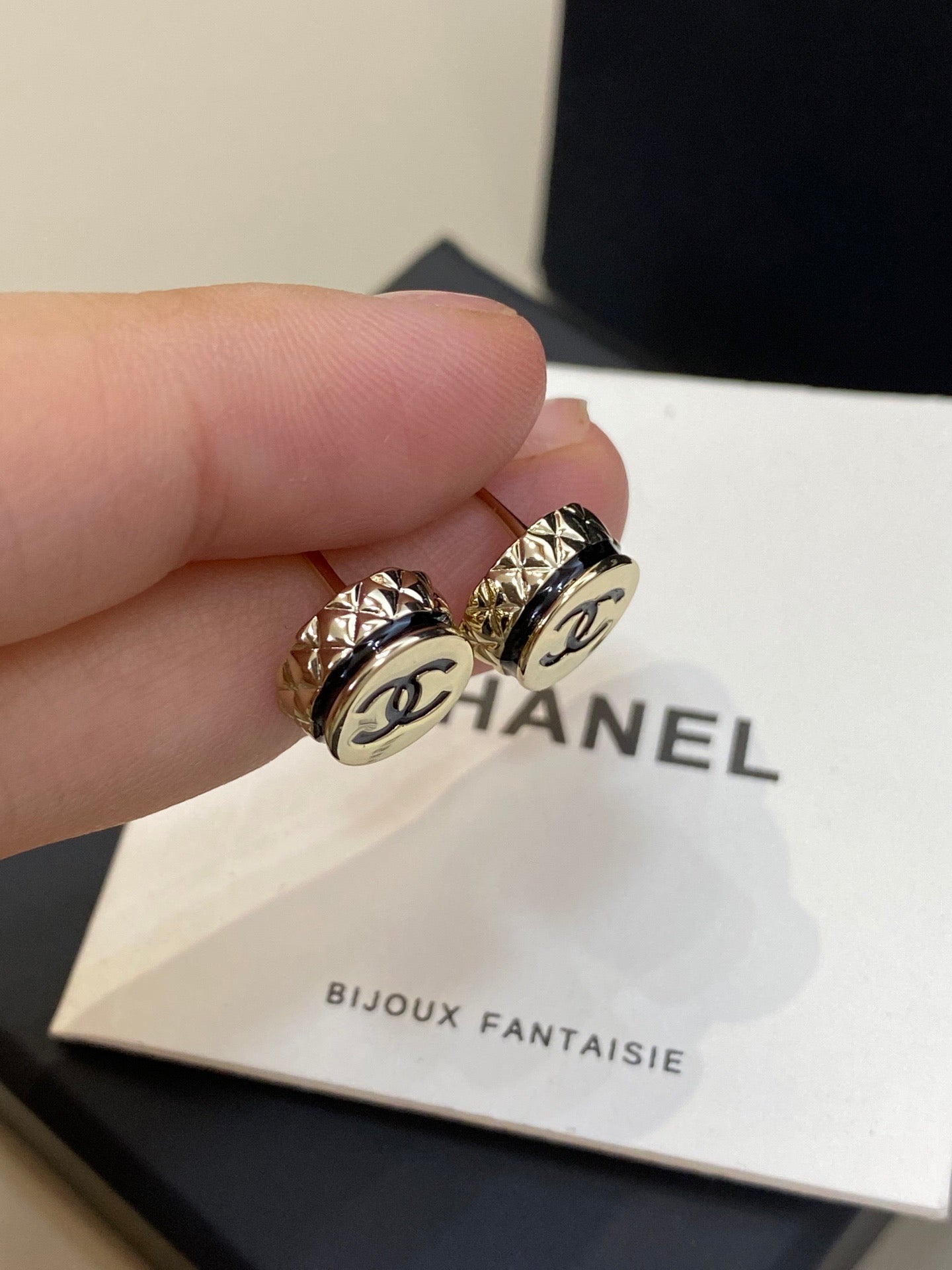 Gold Chanel earrings held by a hand on a Chanel jewelry box.
