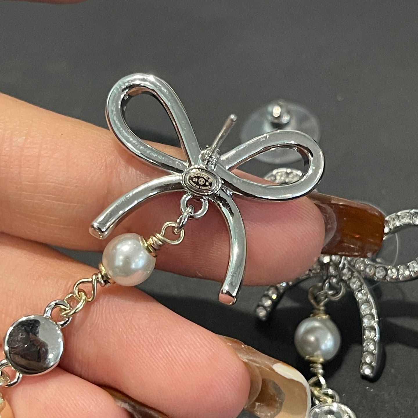 Silver bow-shaped jewelry with pearl beads held by a hand on a dark surface.
