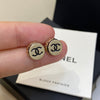 Gold Chanel earrings held by a hand with a Chanel box in the background.