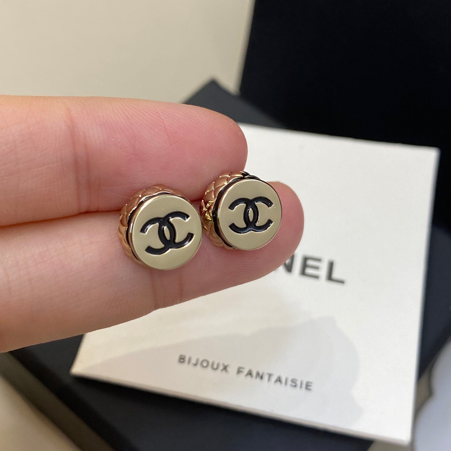 Gold Chanel earrings held by a hand with a Chanel box in the background.