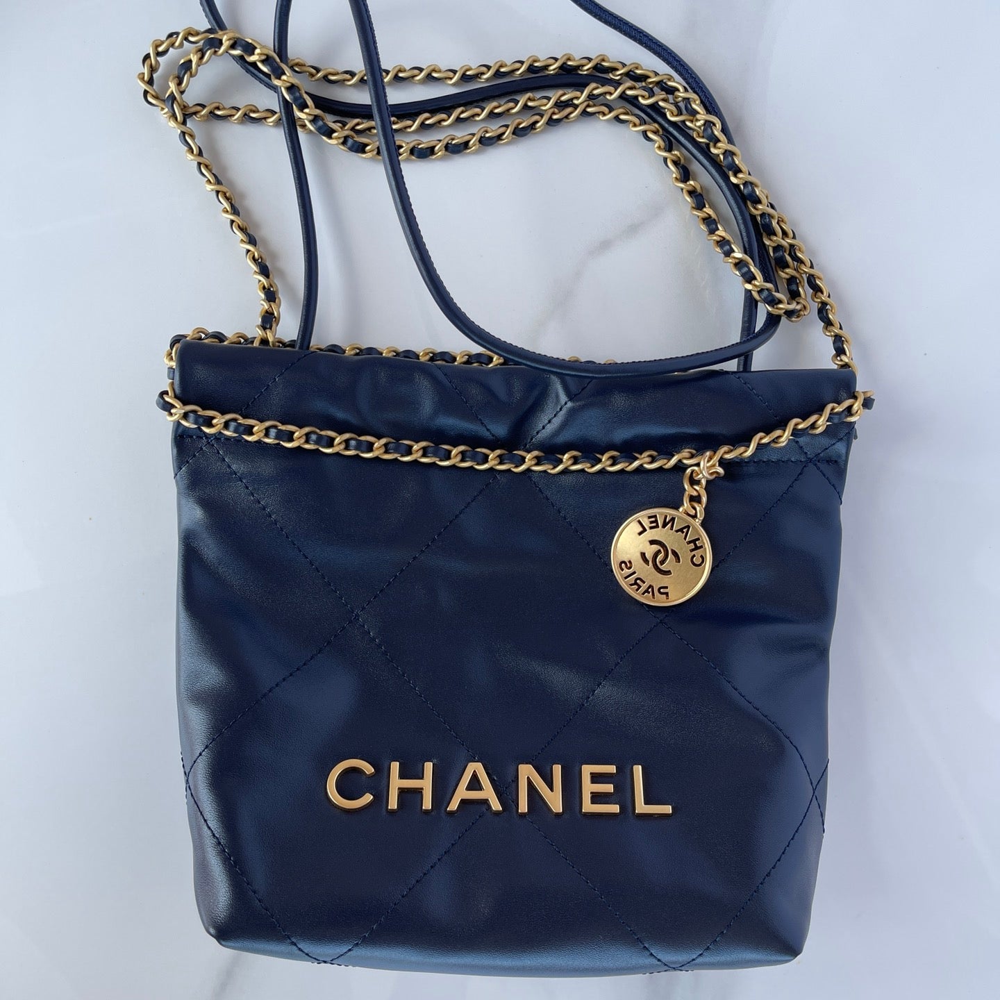 Navy blue Chanel handbag with gold chain strap on a white background