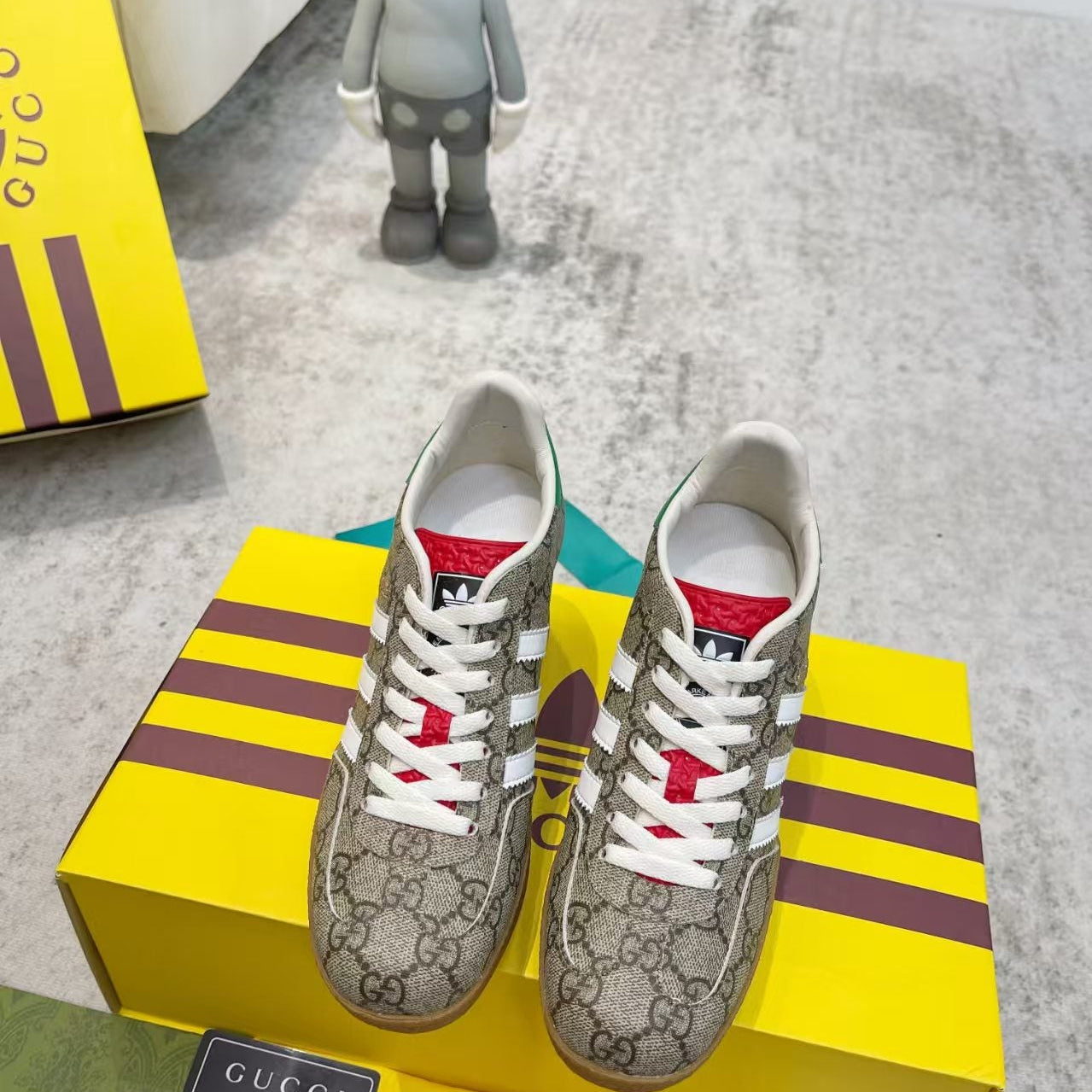 Gray sneakers with white and red accents on a yellow Gucci box.