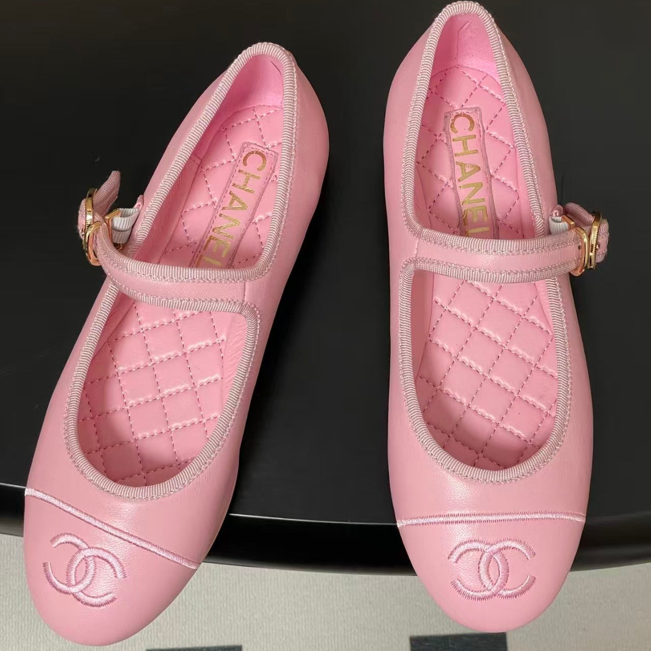 Pair of pink quilted shoes with Chanel logo on a black background